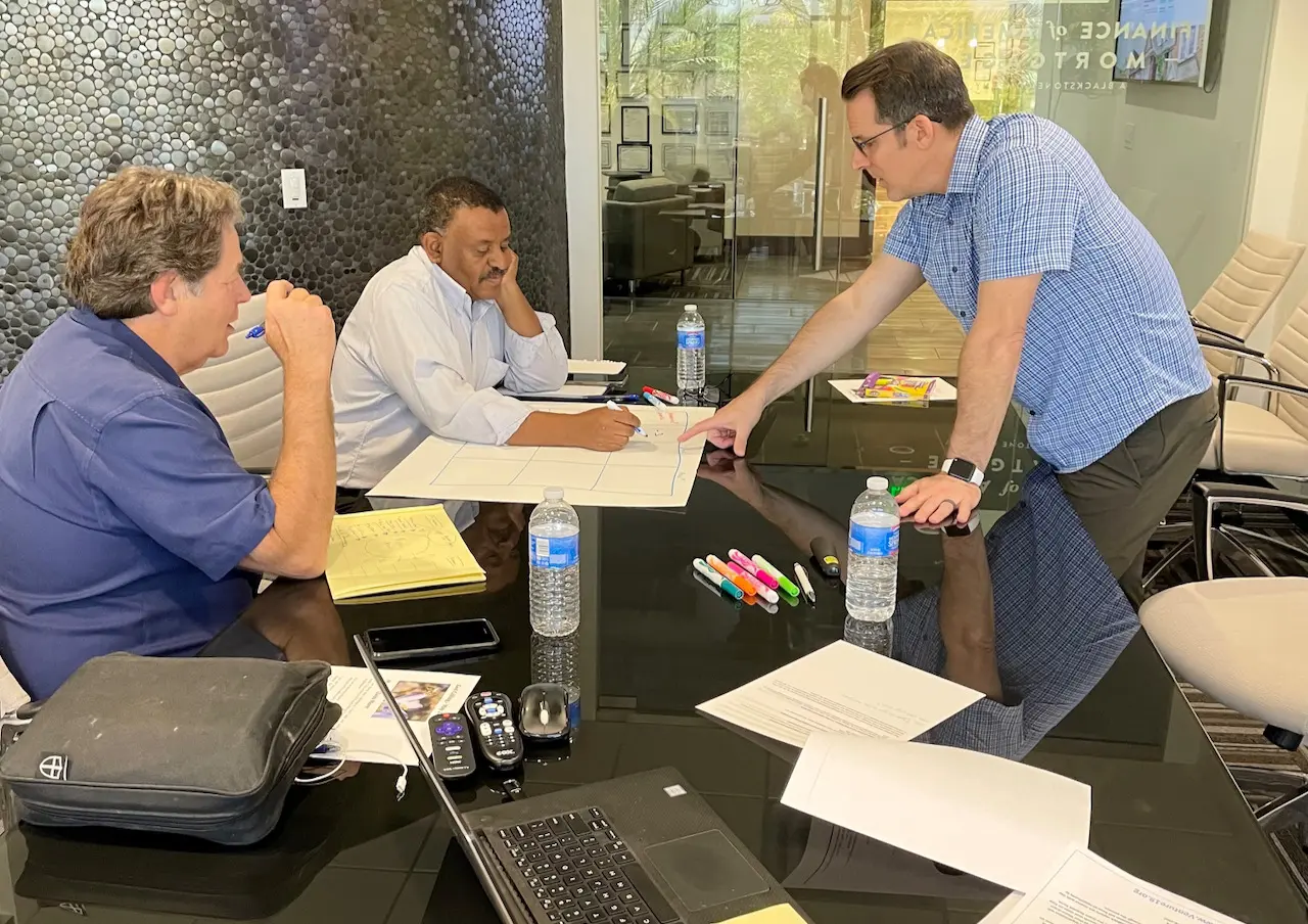 three men sitting while using laptops and watching man beside whiteboard